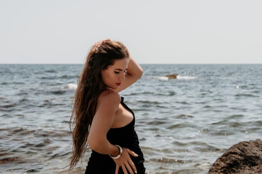 Woman travel sea. Young Happy woman in a long red dress posing on a beach near the sea on background of volcanic rocks, like in Iceland, sharing travel adventure journey