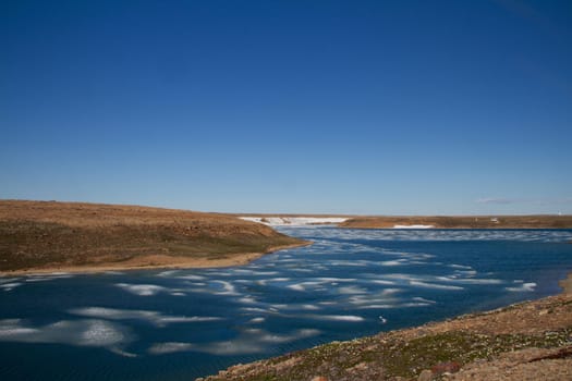 Arctic landscape in summer time. A river with broken ice flowing along a barren tundra. Near Cambridge Bay, Nunavut, Canada