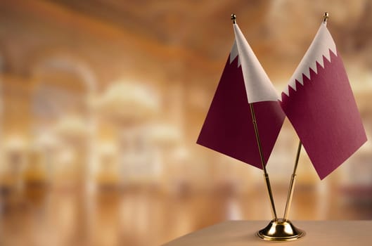 Small flags of the Qatar on an abstract blurry background.