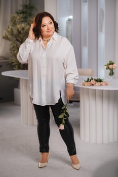 An adult woman in a white shirt holds one rose in her hands while standing in the interior. Pink roses.