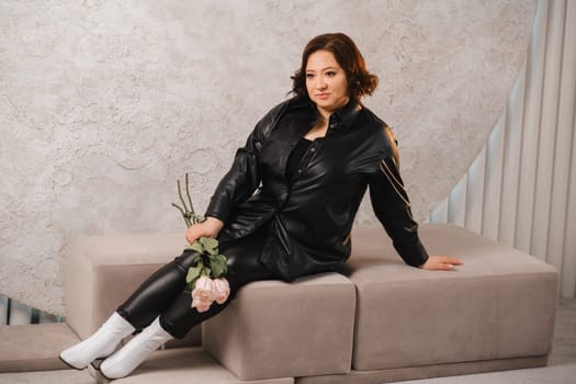 a stylish adult woman in black leather clothes is sitting with a bouquet of pink roses in the interior.