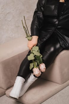 Close-up of legs and a bouquet of flowers of a stylish woman in black leather clothes sitting on an ottoman.