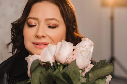 a stylish adult woman in black leather clothes stands with a bouquet of pink roses in the interior.