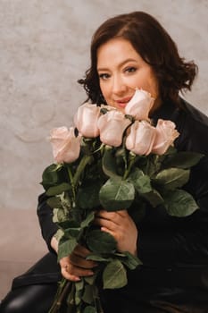 a stylish adult woman in black leather clothes stands with a bouquet of pink roses in the interior.