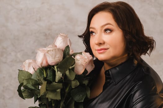 a stylish adult woman in black leather clothes stands with a bouquet of pink roses in the interior.