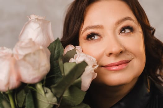 a stylish adult woman in black leather clothes stands with a bouquet of pink roses in the interior.