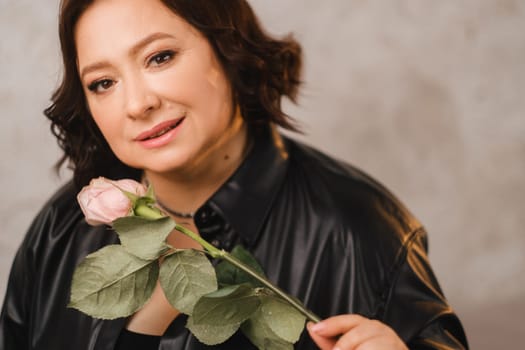 a stylish adult woman in black leather clothes stands with a bouquet of pink roses in the interior.