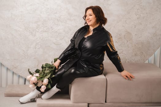 a stylish adult woman in black leather clothes is sitting with a bouquet of pink roses in the interior.