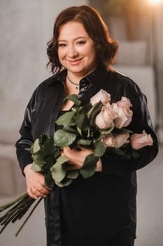 a stylish adult woman in black leather clothes stands with a bouquet of pink roses in the interior.