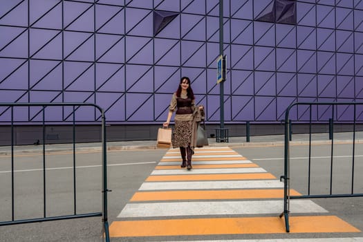 A beautiful girl with shopping bags is walking along a pedestrian crosswalk. Consumerism, shopping, shopping, lifestyle concept.