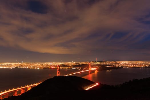 Lights from cars and traffic on Golden Gate Bridge ith sprawling city at night. High quality photo