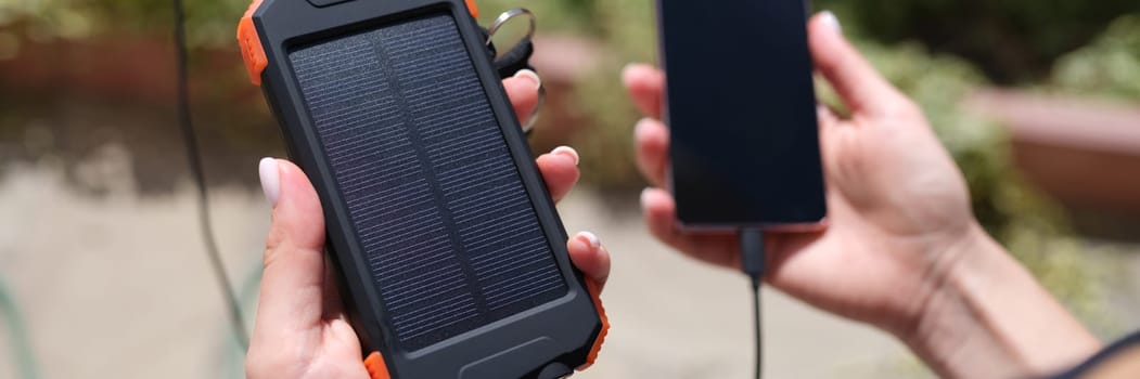 Female hand holding solar power bank and mobile phone closeup. Modern energy-saving devices concept