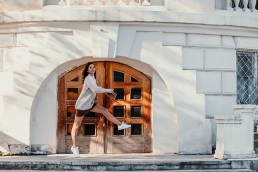 Woman walks in the city, lifestyle. Young beautiful woman in a loose light sweater, brown skirt and sneakers with a hat