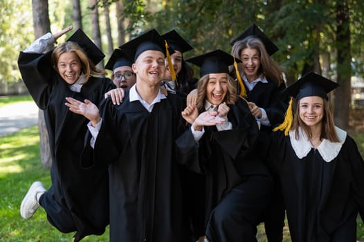 A group of graduates in robes congratulate each other on their graduation outdoors