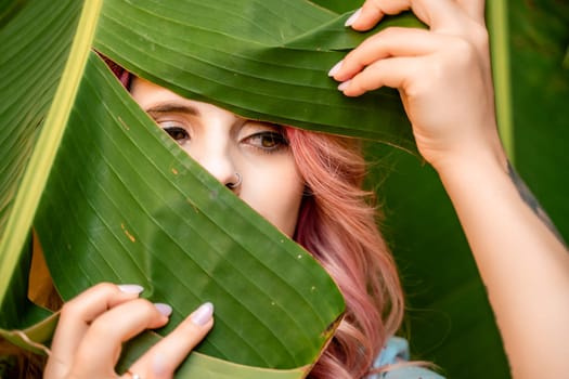 Woman portrait pink hair banana leaf. A beautiful young woman among the huge green leaves of a banana tree