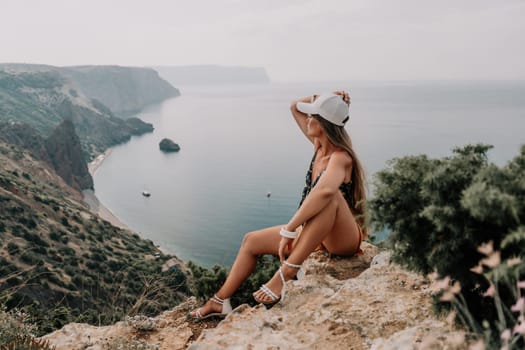 Woman travel sea. Happy tourist taking picture outdoors for memories. Woman traveler looks at the edge of the cliff on the sea bay of mountains, sharing travel adventure journey.