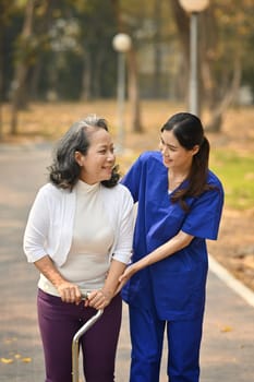 Careful caregiver taking care of elderly woman patient during walking outdoor. Assistance and rehabilitation concept.