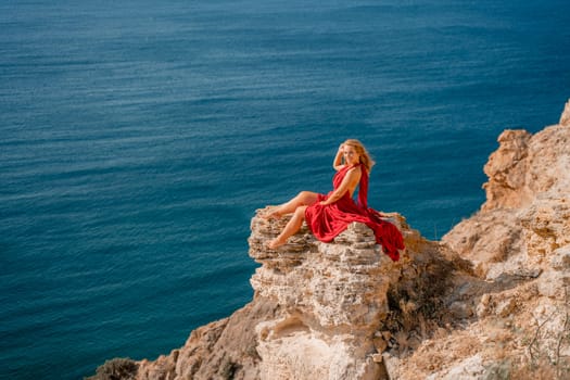 A girl with flowing hair in a long red dress sits on a rock above the sea. The stone can be seen in the sea