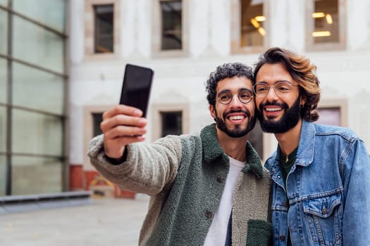happy couple of gay men taking a selfie photo with their mobile phone in the street, concept of urban lifestyle and love between people of the same sex, copy space for text