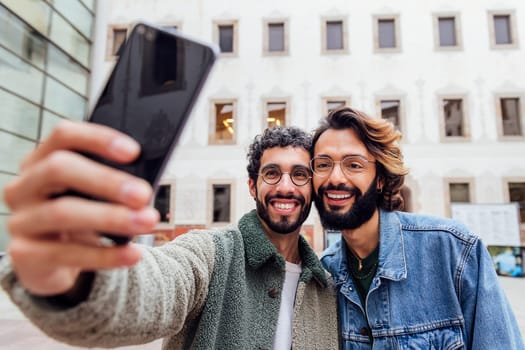 happy couple of gay men laughing taking a selfie photo with a mobile phone in the street, concept of urban lifestyle and love between people of the same sex