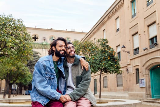 happy couple of gay men sitting in a park holding hands lovingly and tenderly, concept of urban lifestyle and love between people of the same sex