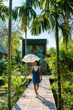 Asian women walk with umbrella at a wooden cottage surrounded by palm trees and a vegetable garden in the countryside. cabin in tropical rainforest