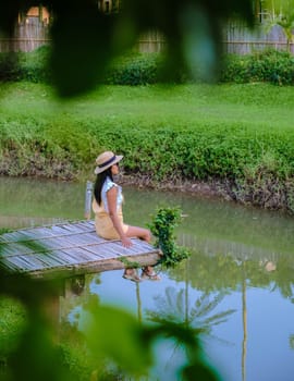 Asian woman with a hat sitting on a wooden pier at the waterfront.