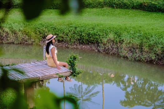 Asian woman with a hat sitting on a wooden pier at the waterfront.