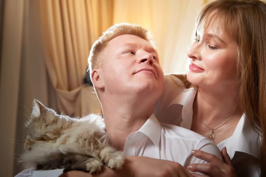 Happy loving couple with big fat fluffy cat in the room