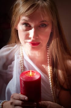 Beautiful arabian girl with candles in red room full of rich fabrics and carpets in sultan harem. Photo shoot of woman an oriental style odalisque. Model poses in sari as caring wife and hostess