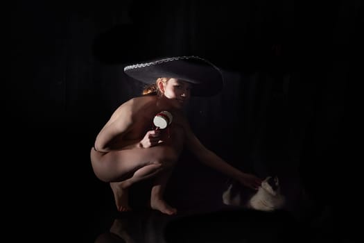 Beautiful slim naked girl in hat and in underwear with domestic cat on a black background in photo studio
