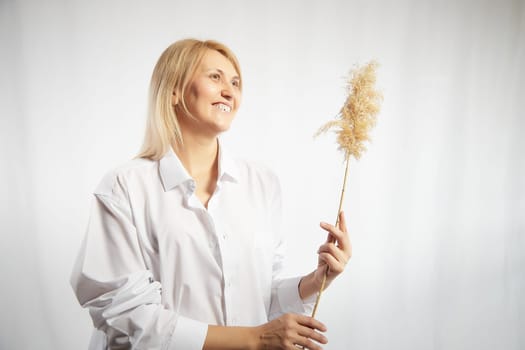 Portrait of a pretty blonde smiling woman with soft ear in hands posing on a white background. Happy girl model in white shirt in studio. The concept of softness, tenderness and dreams