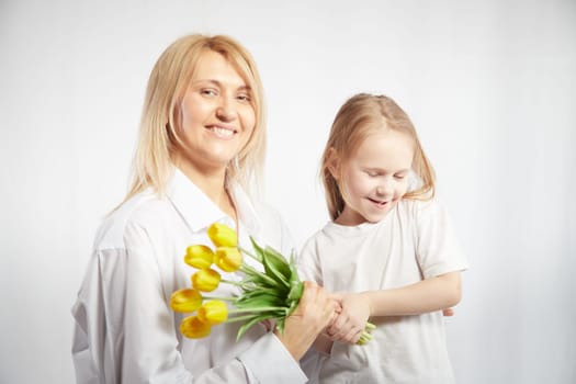 Blonde mother and daughter with a bouquet of tulips on a white background. Mom and girl together on holiday mother's day with flowers. Congratulations to women on International Women's Day on March 8