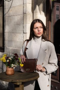 Street style, autumn, spring fashion concept: fashionable woman wearing luxury beige coat, posing in a sunshine near round wooden table