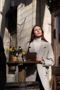 Street style, autumn, spring fashion concept: fashionable woman wearing luxury beige coat, posing in a sunshine near round wooden table