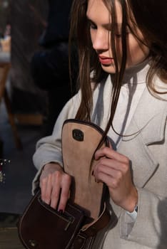 Street style, autumn, spring fashion concept: fashionable woman wearing luxury beige coat, posing in a sunshine near round wooden table