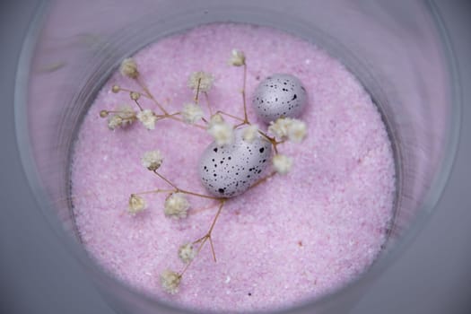 A glass with Easter eggs on pink sand background, holiday decoration. High quality photo