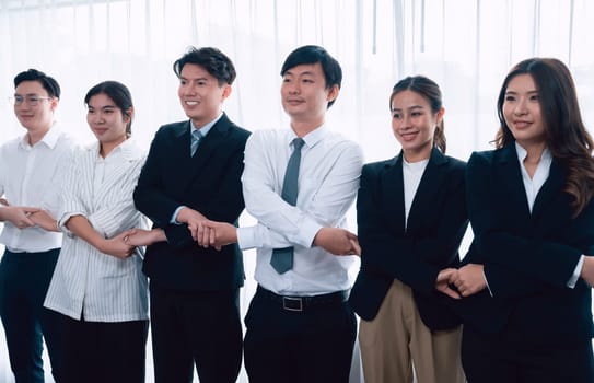 Cohesive group of businesspeople standing in row, holding hand in line together after meeting to promote harmony in workplace. Asian office workers strong teamwork and unity concept.