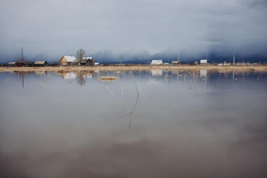 Mirror reflection from the water of melted snow in a Buryat village in dense fog against the backdrop of the Sayan Mountains