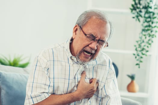 An agonizing senior man suffering from chest pain or heart attack alone in his living room. Serious health problem and feeling unwell concept for seniors.
