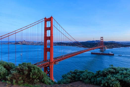 Cargo ship sails into San Francisco Bay under Golden Gate Bridge at sunset. High quality photo