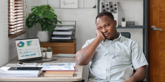 Tired American African business man in stress works with many paperwork document. migraine attack. Freelance, work from home.