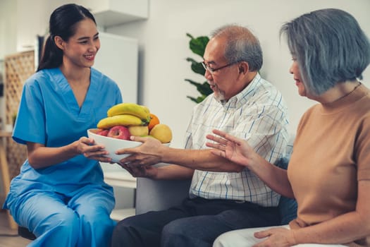 Contented senior couple taking a bowl of fruit from a nurse at home. Senior care at home.