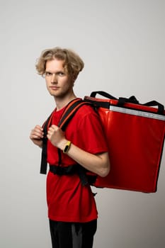 Side view of young courier in a red uniform and with a thermo bag on color red background, space for text. Fast express home delivery. Online order
