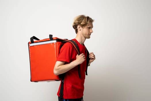Handsome young delivery man posing with thermo backpack delivery food to client on white background. Courier male