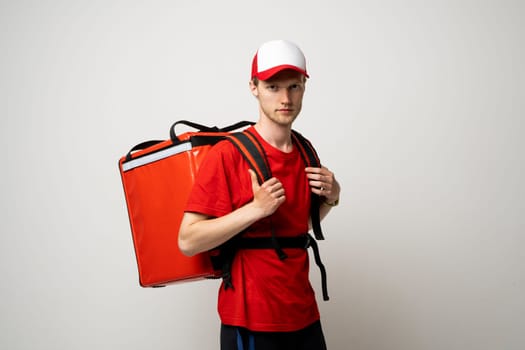 Young courier delivery man in red uniform with thermo backpack on white background. Fast express home delivery. Online order