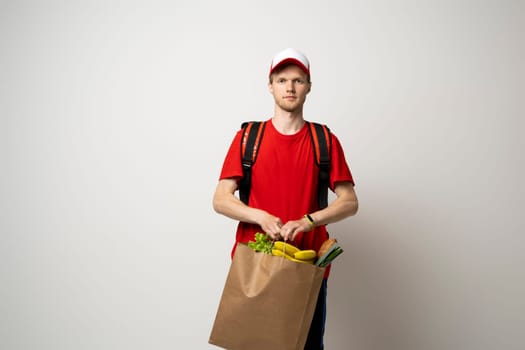 Food shipping, profession and people concept. Delivery man in red uniforn holding a paper bag full of vegetables