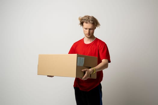 Delivery man in red uniform carry cardboard box in hands on white background. Delivery guy give parcel shipment