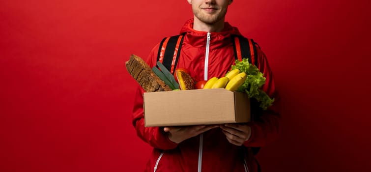 Grocery delivery courier in red uniform with a paper box with food showing a thumb up. Thumb up gesture. Food delivery service concept
