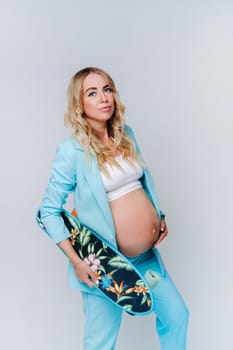 a pregnant girl in turquoise clothes with a skateboard in her hands on a gray background.